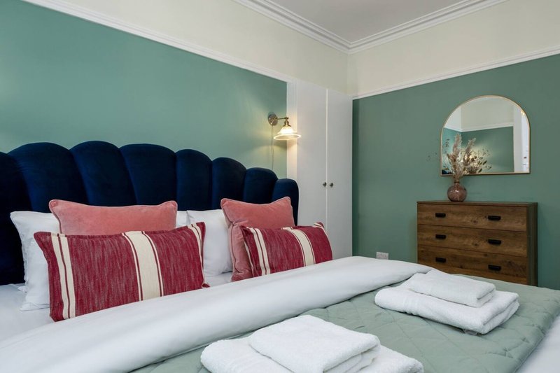 Bedroom with teal feature wall, navy velvet headboard, red striped pillows and white bedding