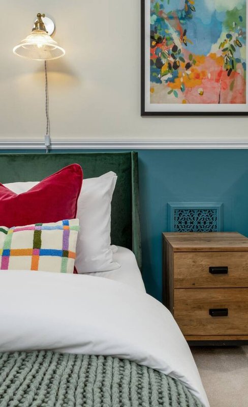 Bedroom with double bed, colorful pillows, wooden nightstand, and pendant lamp