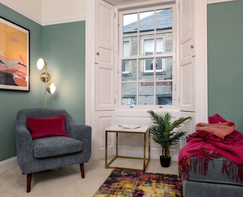 Modern bedroom with armchair, bed with red cushions, desk, plant and large window