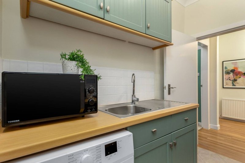 Modern kitchen with green cabinetry, wooden countertop, microwave and sink