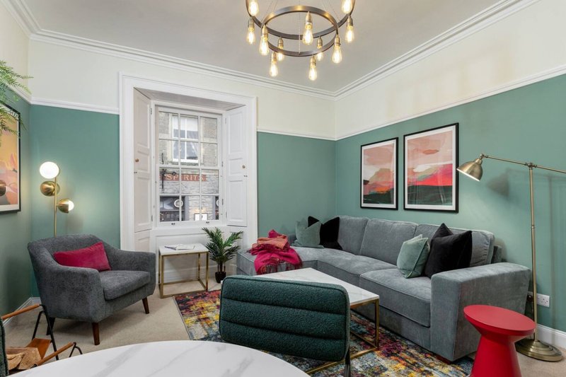 Bright living room with teal walls, gray sofa and armchair, framed artwork, and pendant ceiling light