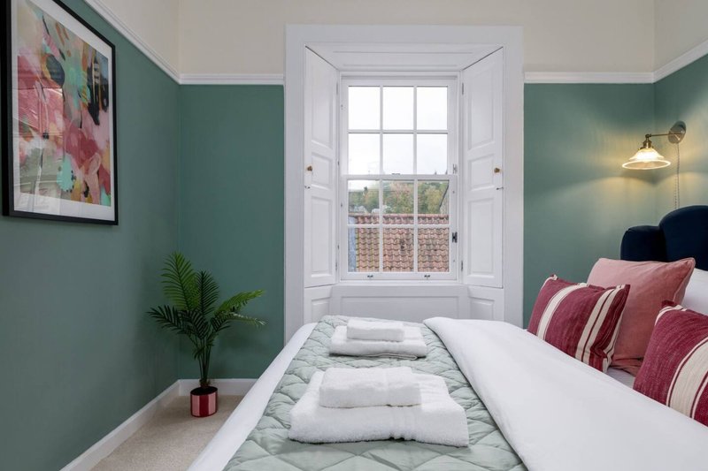 Bedroom with green walls, white double doors, bed with pink pillows and folded towels