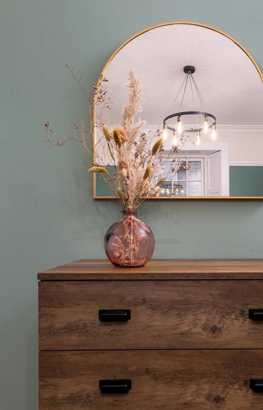 Bedroom dresser with dried flowers in pink vase, round mirror, pendant light fixture