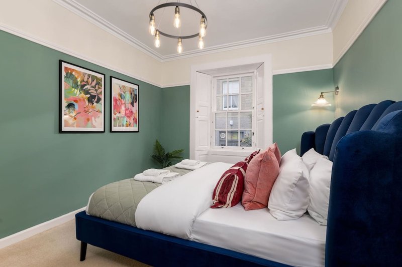 Bedroom with green walls, double bed with navy headboard, floral artwork and ceiling light fixture