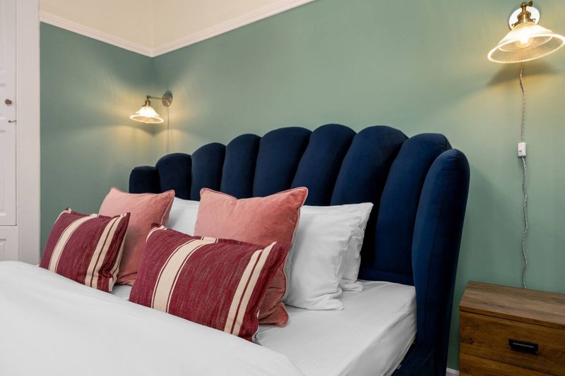 Bedroom with dark blue upholstered headboard, pink and burgundy pillows, white bedding, and sage green wall