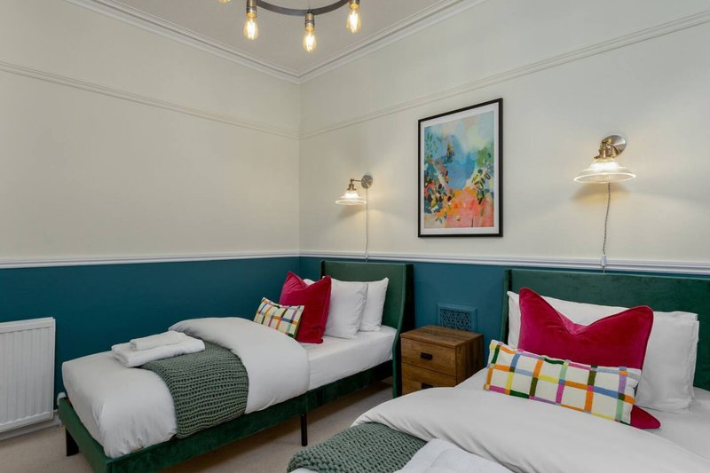 Twin bedroom with teal panelled walls, white bedding, colourful cushions and pendant lighting