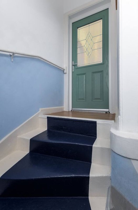 Staircase with black steps, blue and white walls, green front door with window