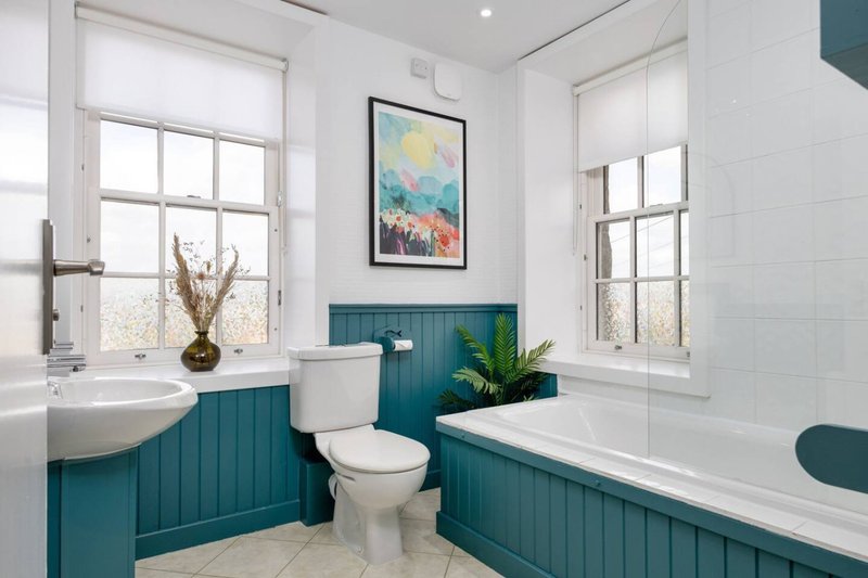 Bright bathroom with teal paneling, white sink, toilet, bathtub and framed artwork