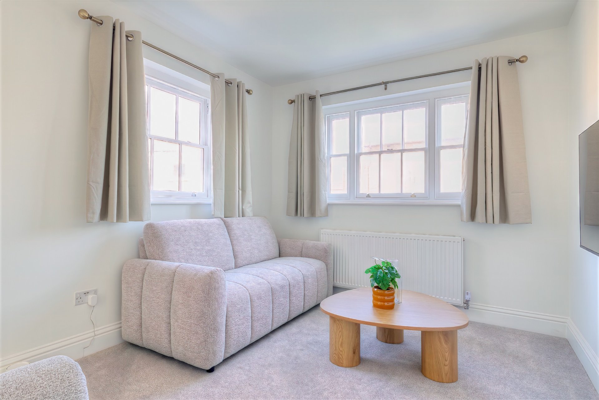 Bright living room with purple armchair, wooden coffee table, and two large windows with cream curtains