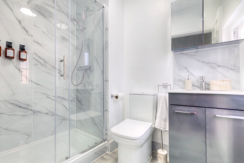 Modern bathroom with marble tiles, glass shower enclosure, toilet, and vanity sink