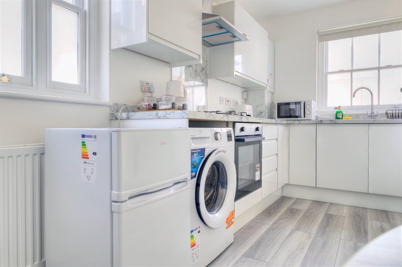 Clean modern kitchen with white cabinetry, washing machine, oven, refrigerator and natural light