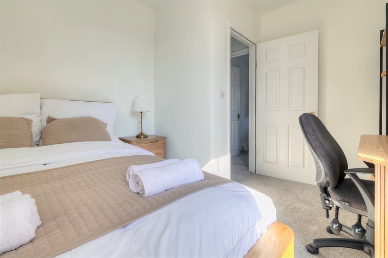 Bedroom with two beds, wooden headboards, bedside lamp, desk chair and wardrobe