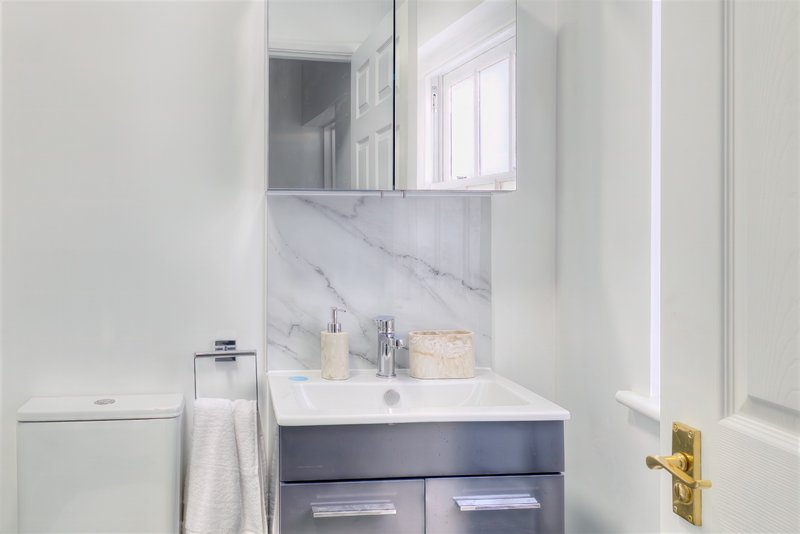 Modern bathroom with marble backsplash, white sink, dark vanity cabinet and mirror