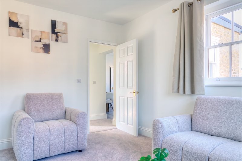 Bright living room with grey upholstered armchair and sofa, abstract wall art, open doorway and large window