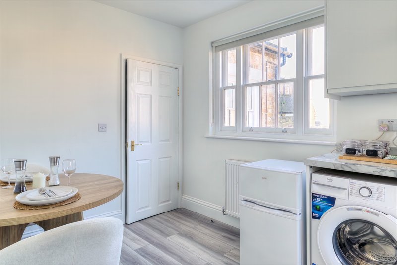 Modern kitchen with white appliances, wooden dining table, window and washing machine