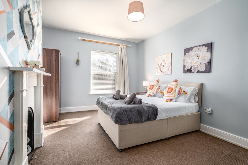 Bright bedroom with double bed, grey bedding, floral wall art, window and ceiling light