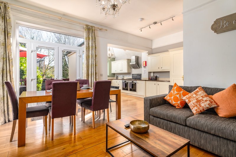 Open-plan living room with dining table, sofa with orange cushions, and kitchen area beyond