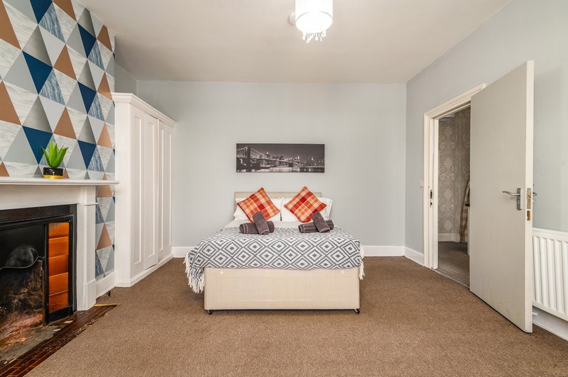 Bedroom with double bed, geometric wall feature, fireplace and carpet flooring