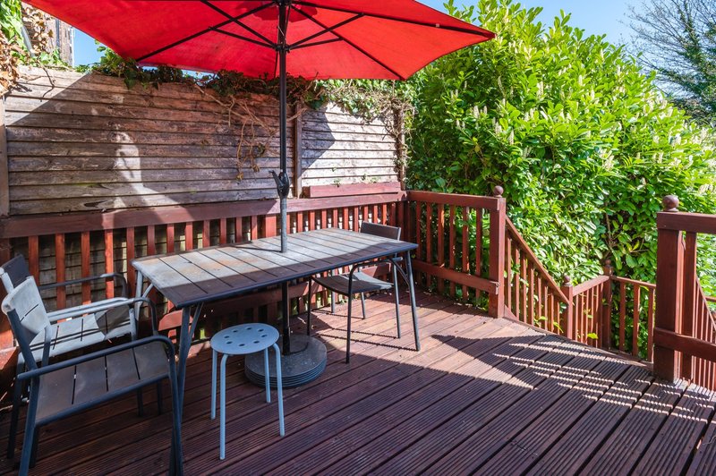 Wooden deck with dining table, chairs, red umbrella and wooden fence railing