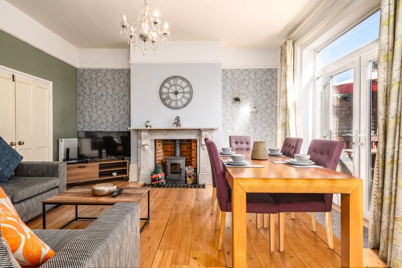 Living room with fireplace, wooden dining table, grey sofa and French doors to garden