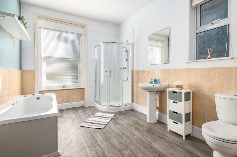 Modern bathroom with corner shower, bathtub, pedestal sink, toilet and window