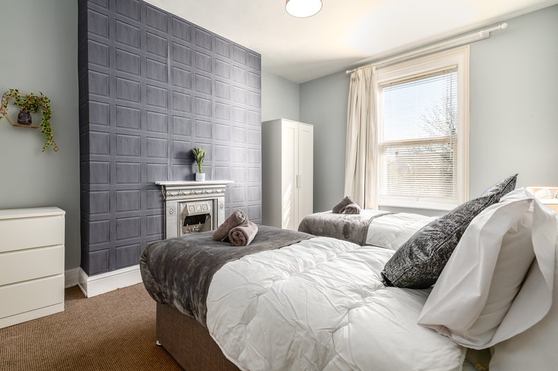 Bright bedroom with two single beds, grey feature wall, fireplace and large window