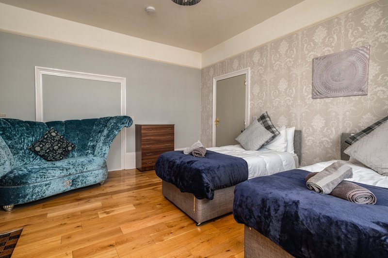 Bedroom with two beds, teal velvet sofa, wooden floor and patterned wallpaper