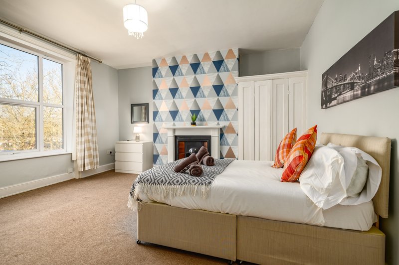 Spacious bedroom with double bed, fireplace, geometric wallpaper accent wall, and large window
