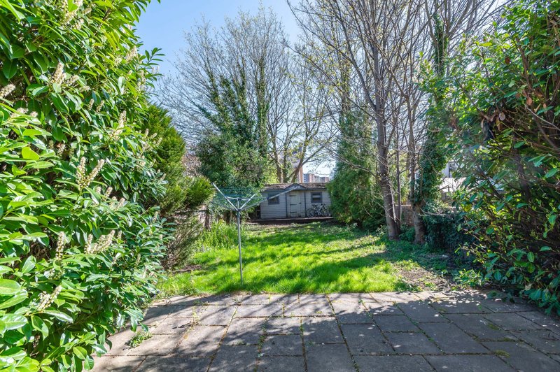 Garden view with paved patio, green lawn, trees and caravan in background
