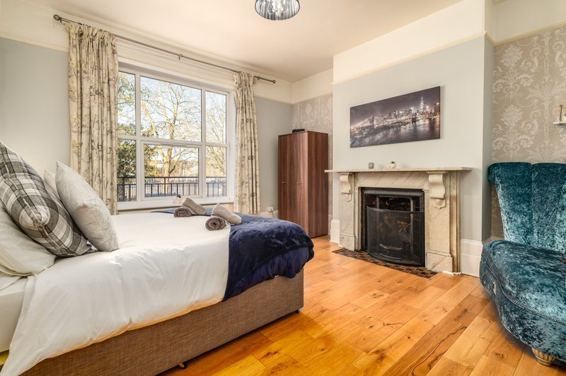 Bedroom with double bed, fireplace, armchair, wooden floor and large window