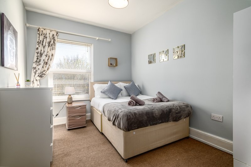 Bright bedroom with double bed, wooden nightstand, window with patterned curtains and carpet flooring