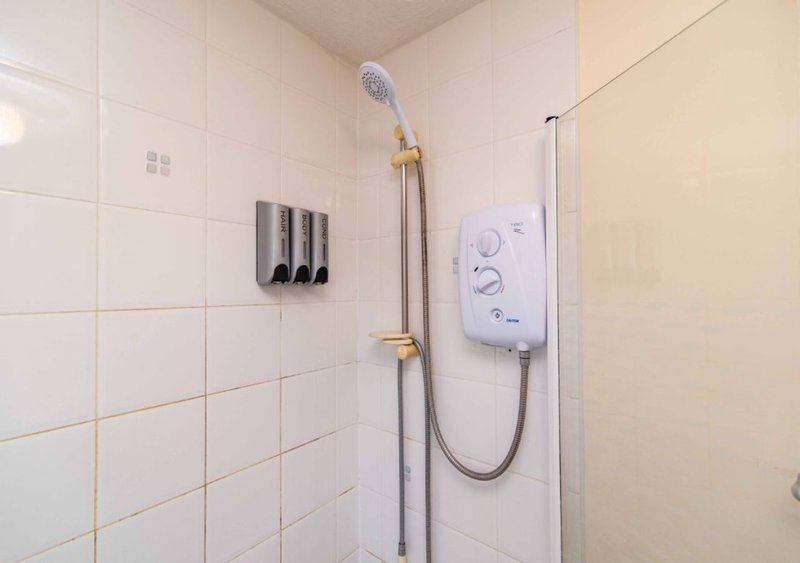 Bathroom with white tile walls, showerhead, brass fixtures and electric shower unit