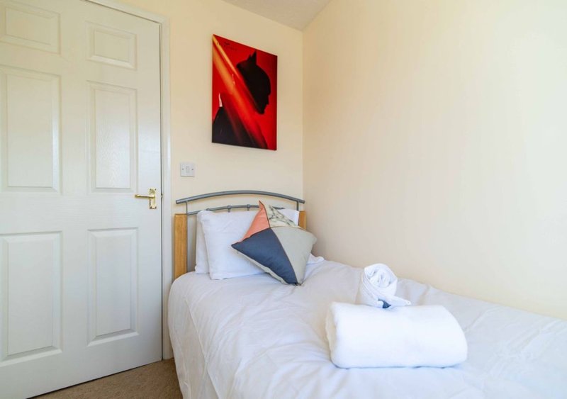 Compact bedroom with single bed, white bedding, colored cushions and abstract wall art