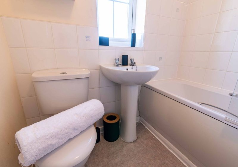 Bright bathroom with white tiles, toilet, pedestal sink, bathtub and window