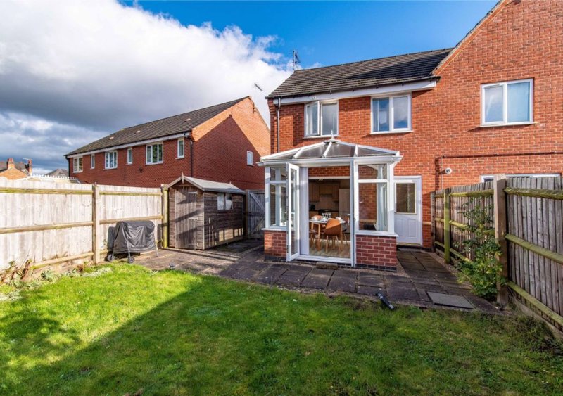 Red brick two-story house with rear garden, patio extension, and wooden fencing