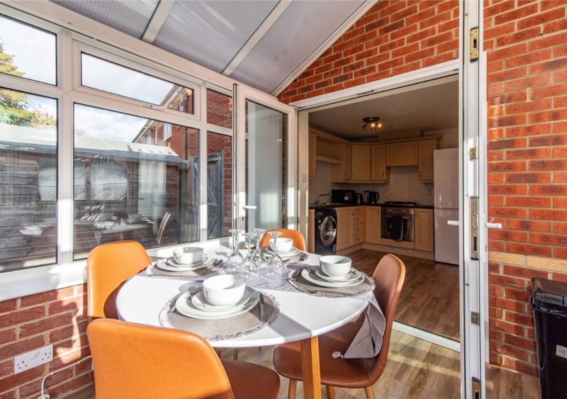 Dining area with round white table, orange chairs, place settings, and view into kitchen