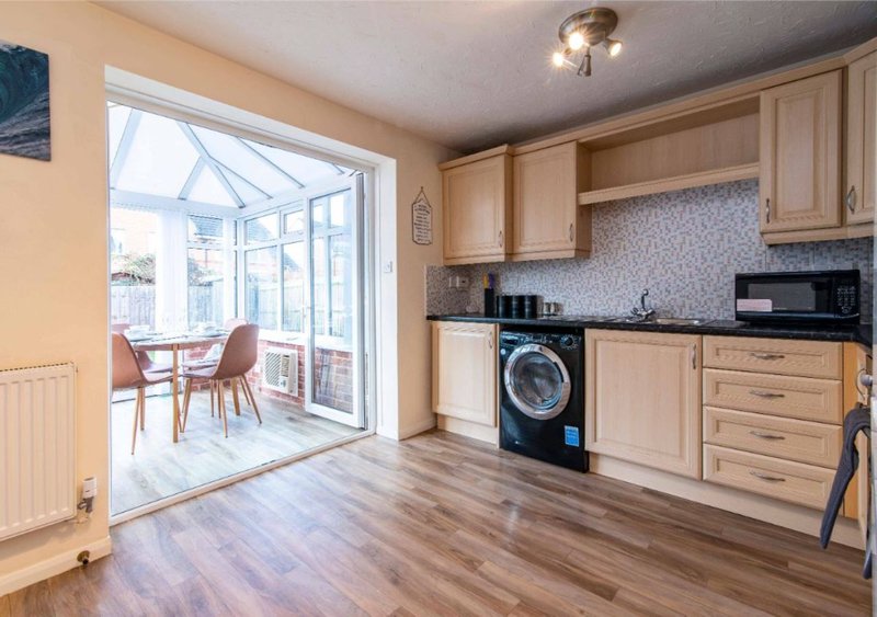 Modern kitchen with wooden cabinets, black washing machine, and glass doors opening to conservatory
