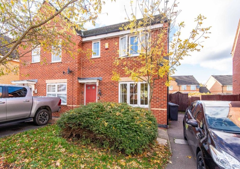 Red brick semi-detached house with driveway, parked vehicles, and autumn foliage