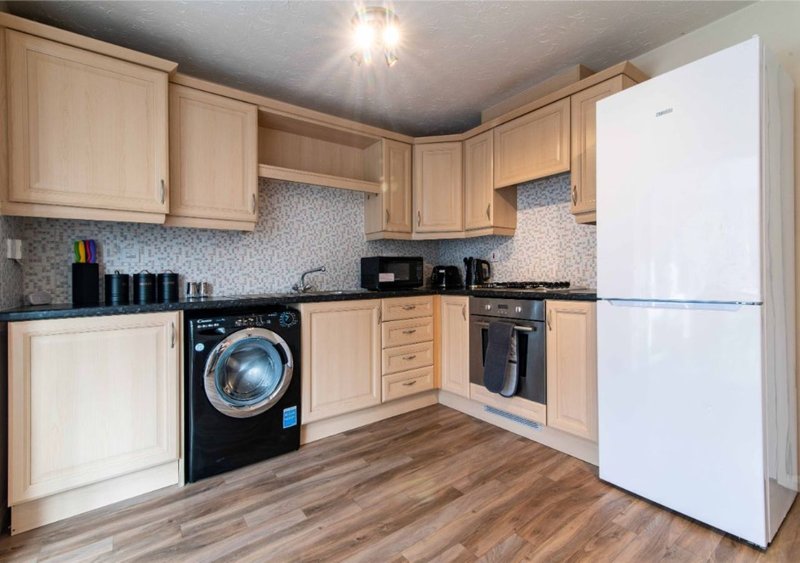 Modern kitchen with light wood cabinets, black appliances, white refrigerator and washing machine