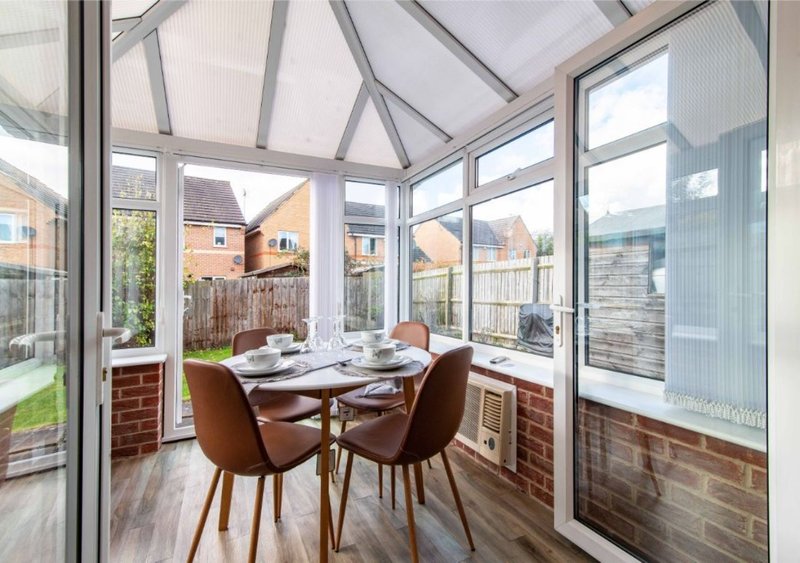 Bright conservatory with dining table, two brown chairs and garden views