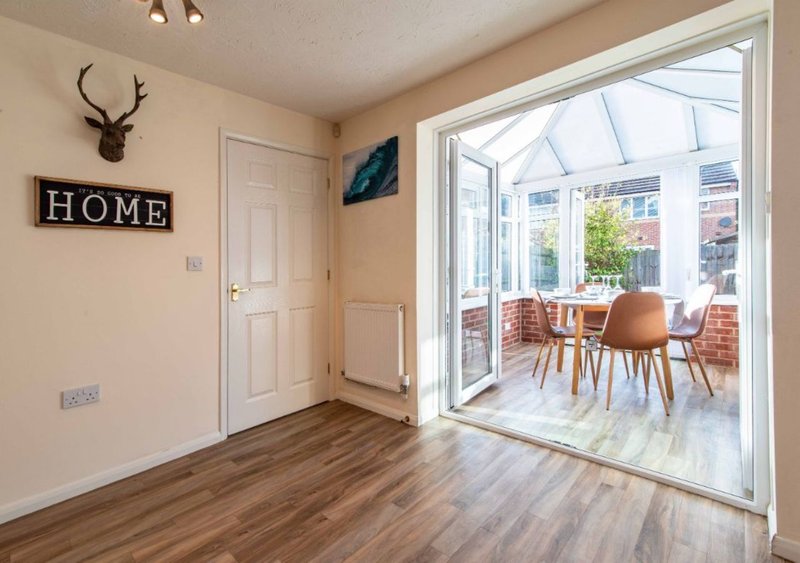 Hallway with wooden floor, cream walls, deer antler mount, and view to conservatory with dining table