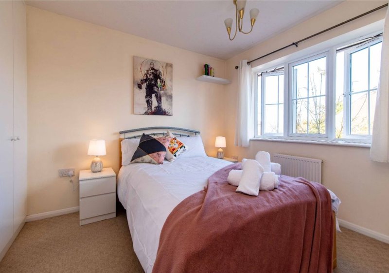 Bright bedroom with double bed, white bedding, burgundy throw, bedside lamps and wall art