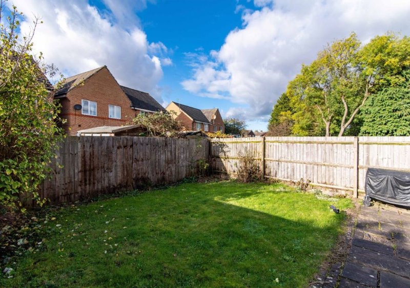Suburban garden with lawn, wooden fence, brick house and neighbouring properties visible
