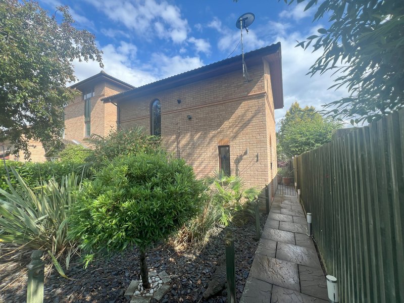 Brick house exterior with landscaped garden, pathway and green fence