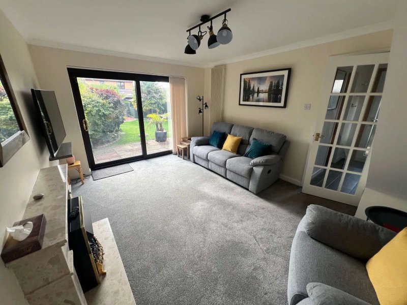 Bright living room with grey carpet, two sofas, large patio doors overlooking garden