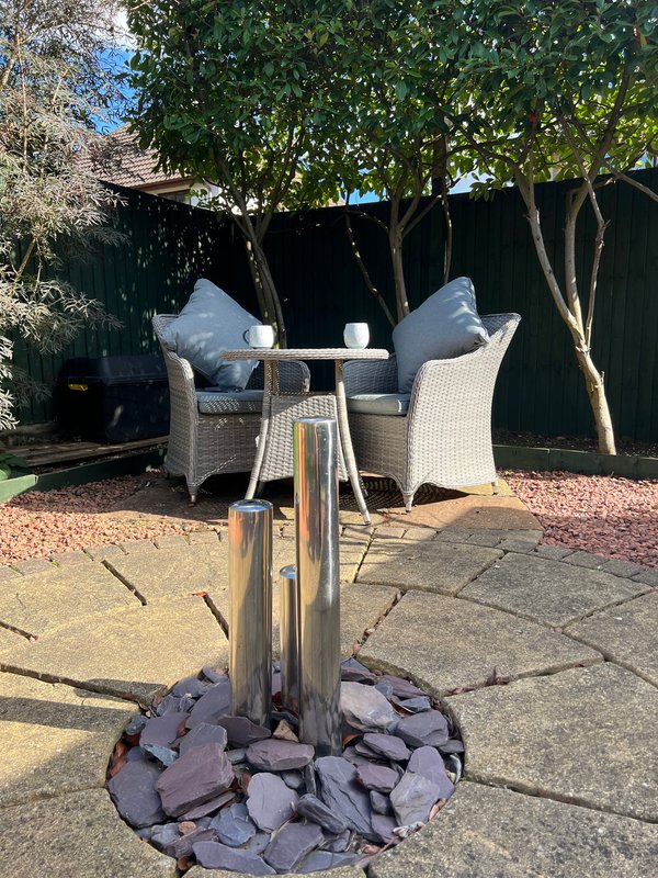 Patio area with rattan seating, umbrella stand, and garden furniture under trees
