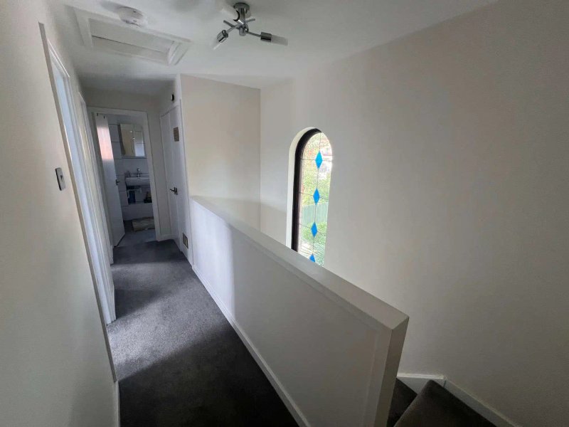 Bright hallway with white walls, ceiling fan, decorative window and grey carpet flooring