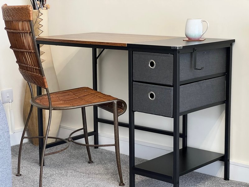 Workspace with black desk, wooden chair, white pitcher, and woven basket organizer
