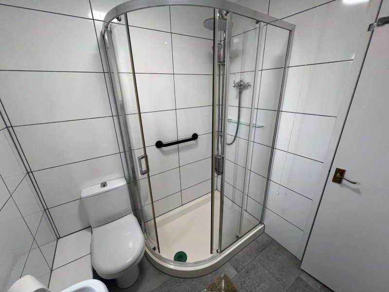 Modern bathroom with corner shower cubicle, toilet, white tile walls and grey floor