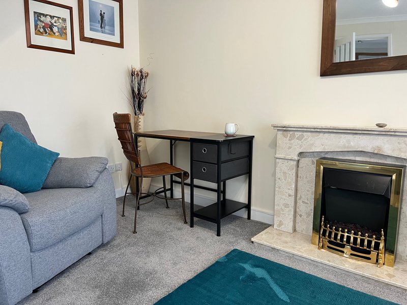 Living room with blue armchair, desk, fireplace with brass insert, and framed wall art
